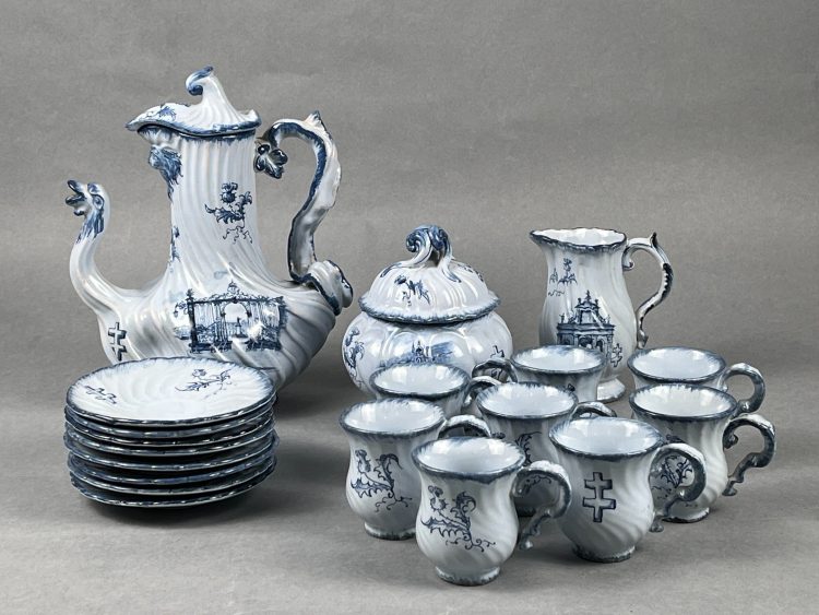 Emile GALLE (Lorraine). Service héraldique-Nancy. Service à café se composant de 8 tasses avec leurs soucoupes, d’un pot à lait, d’un sucrier couvert et d’une cafetière en faïence émaillée blanc-bleu à décor de chardon et de croix de Lorraine, des grilles de la place Stanislas, de la porterie du Palais ducal et de la porte Saint Georges. Vers 1878-1880. Signature manuscrite « E. Gallé Nancy » en bleu. Pas d’accident constaté. Gallé fut un ardent défenseur de la porte Saint-Georges et milita avec succès, en 1878, contre sa destruction. Provenance : collection Geneviève Aubry (1948-2025), Rosières-aux-Salines.